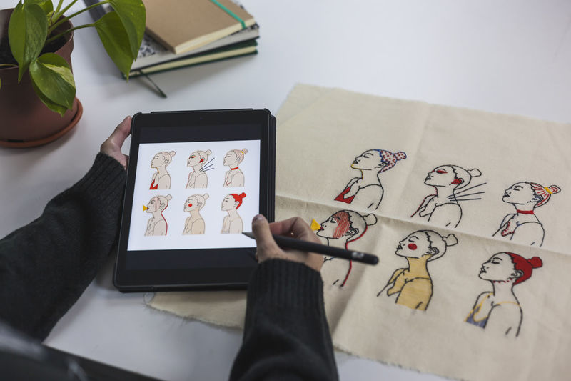 Young freelance woman observing drawing pattern on her digital tablet to do embroidery at studio