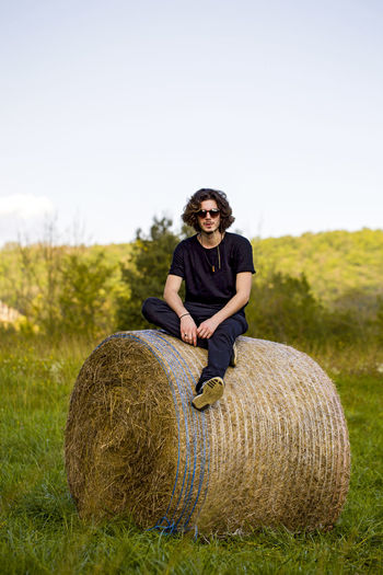 Portrait of man sitting on hay bale against sky