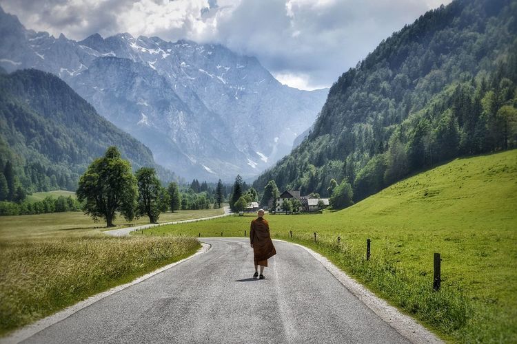 Rear view of monk walking country road leading towards mountains