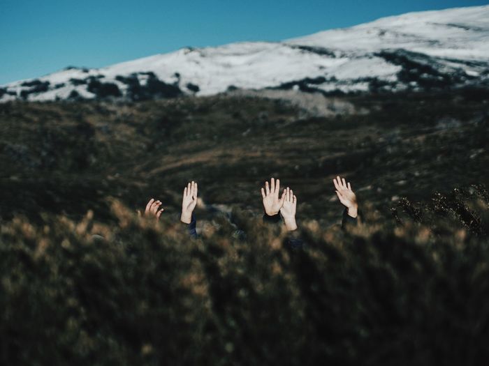 Hands coming out from field against snowcapped mountains