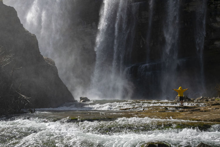 Man standing against scenic waterfall