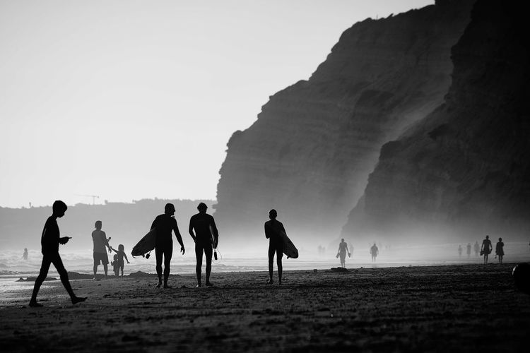 Silhouette people with surfboards at beach against sky 