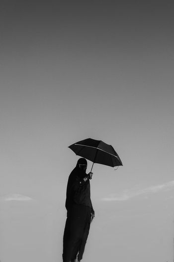 Woman holding umbrella standing against sky during rainy season