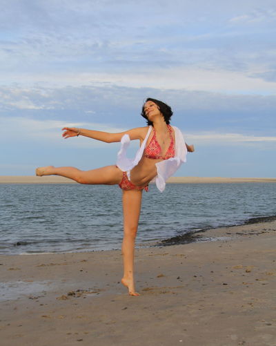 Full length of young woman in bikini dancing on beach