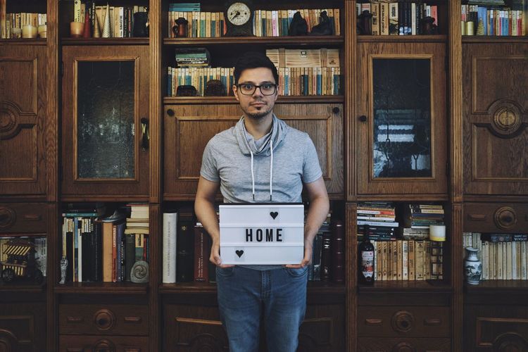 Portrait of man holding home text against shelves