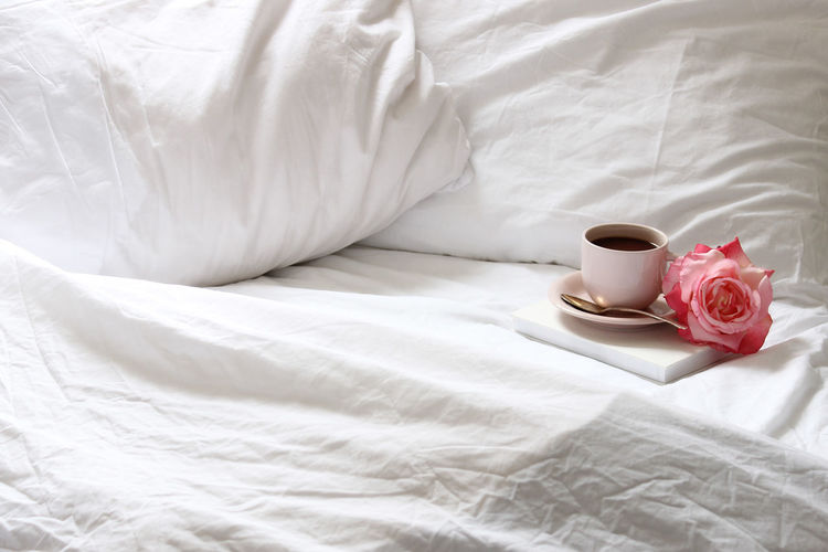 Coffee cup and rose on bed at home