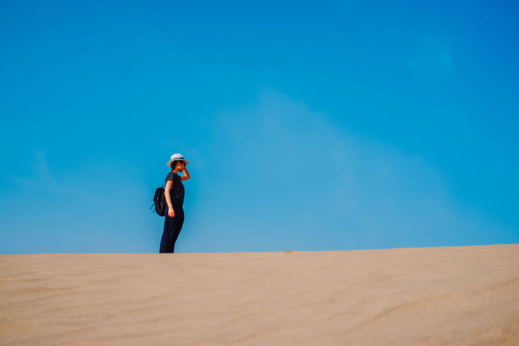 Woman standing on desert against blue sky