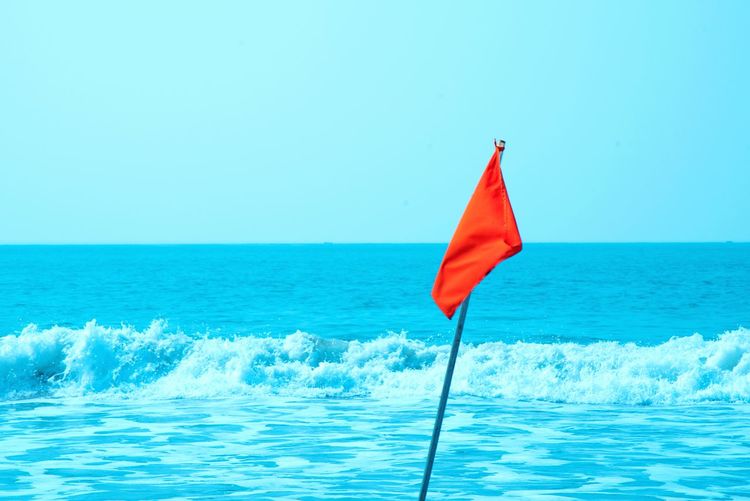 Red flag on blue sea against clear sky