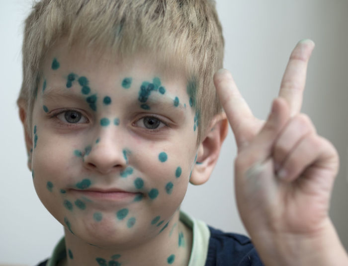 Close-up portrait of cute boy with face paint gesturing peace sign at home