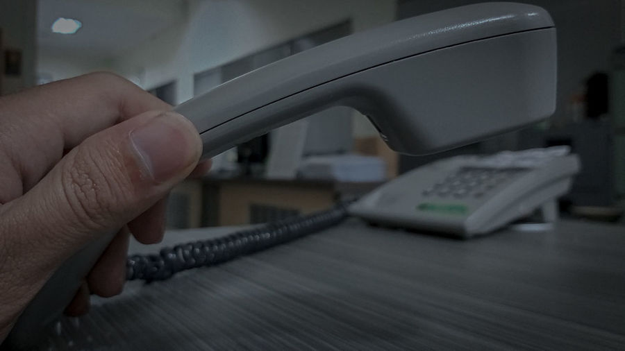 Close-up of man holding landline phone at office desk