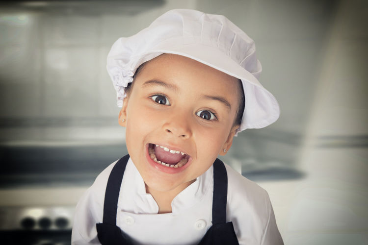 Portrait of girl wearing chef standing in kitchen