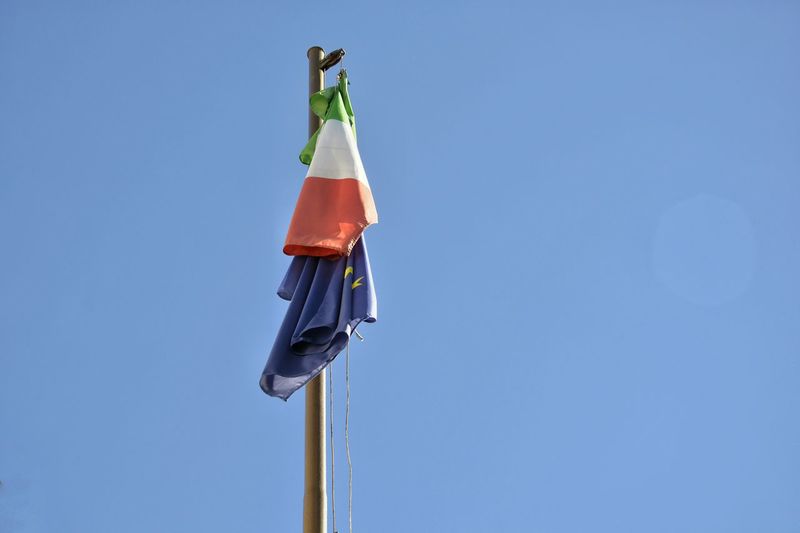 Low angle view of flags on pole against clear blue sky