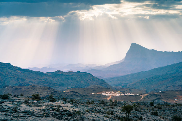 Rays of sunlight shine through scattered clouds on small village in jebel shams , oman. 