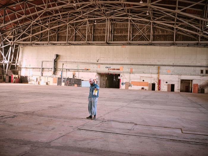 A man dressed in denim holds a can of paint in a large airplane hanger
