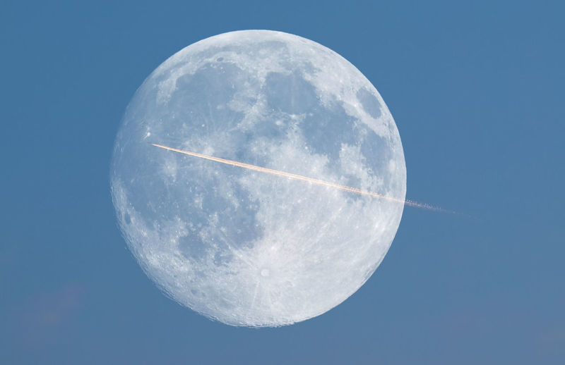 Low angle view of vapor trail against full moon at dusk