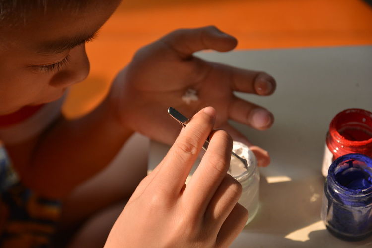 High angle view of boy holding tweezers in paint bottles on table