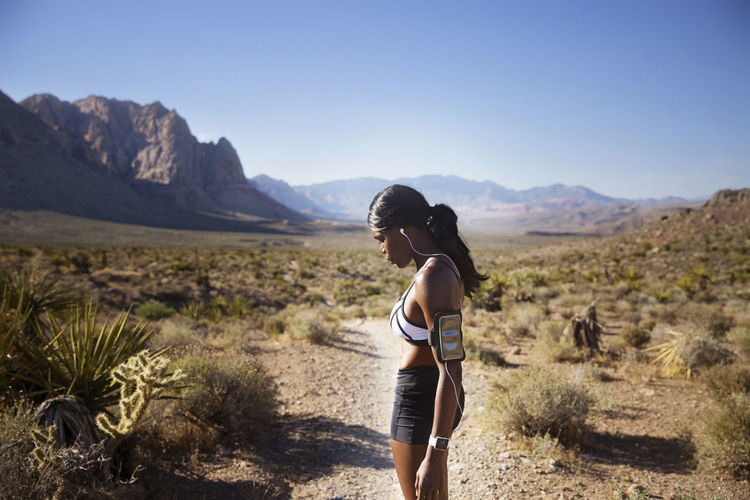 Side view of female athlete standing on dirt road against clear sky