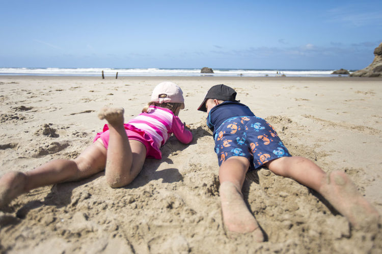 Brother and sister laying down in the sand, watching the ocean.