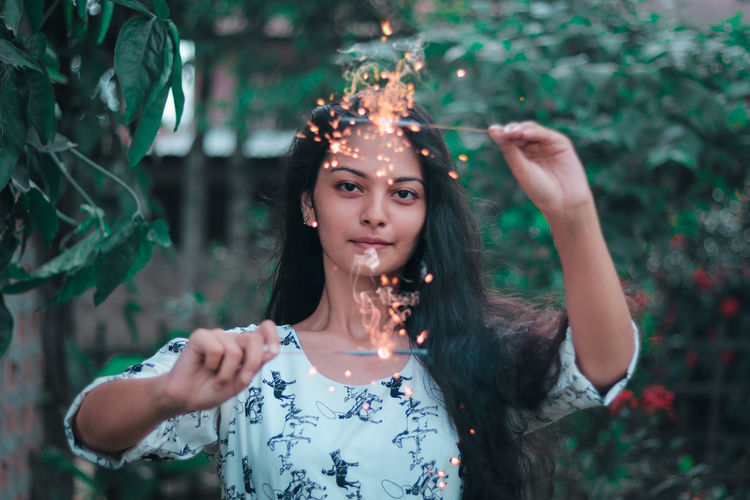 Portrait of girl holding illuminated sparklers against plants