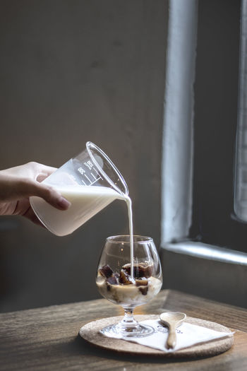 Cropped hand pouring milk in wineglass with ice cubes on table