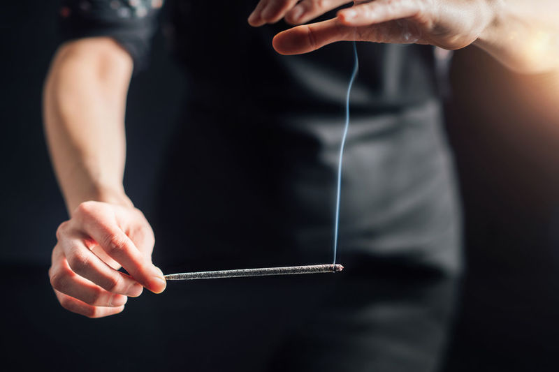 Hands holding a burning incense stick, black background