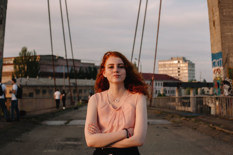 Portrait of young woman with arms crossed standing on bridge in city