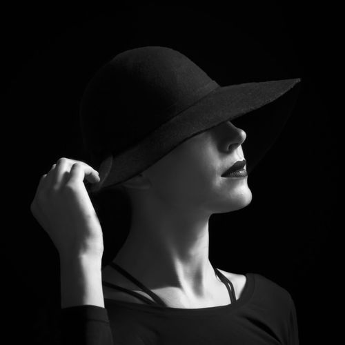 Close-up of young woman wearing hat against black background