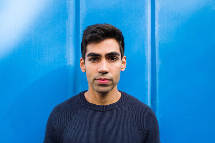 Portrait of the young man looking at the camera standing against blue background