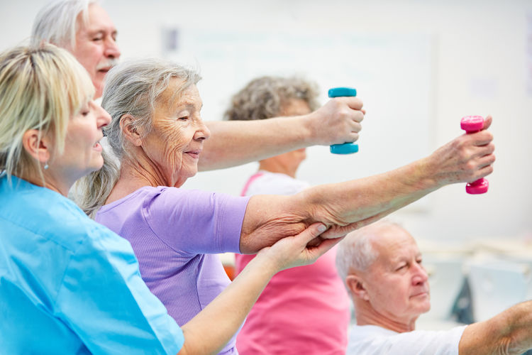 Healthcare nurse guiding senior adults while exercising at fitness class in nursing home