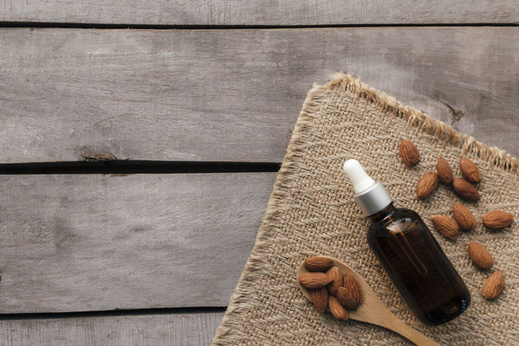 Almond essential oil in glass bottle with spoon. cosmetic on wooden background with sackcloth