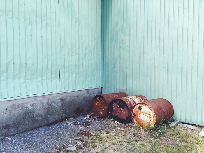 Rusty metallic barrels against turquoise corrugated iron