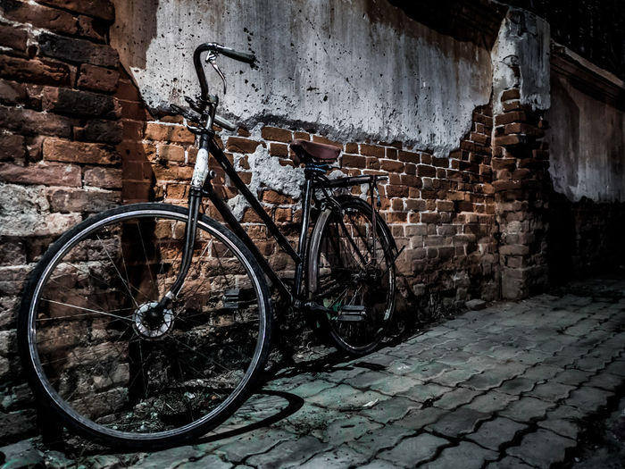 Bicycle parked against weathered brick wall in alley