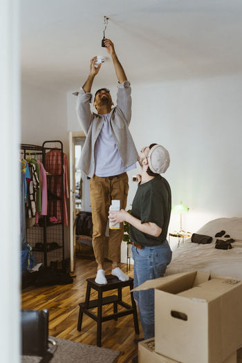 Man installing bulb while standing on stool with boyfriend in living room at home