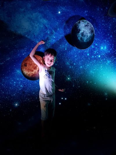 Portrait of smiling boy flexing muscles while standing against space pattern wall