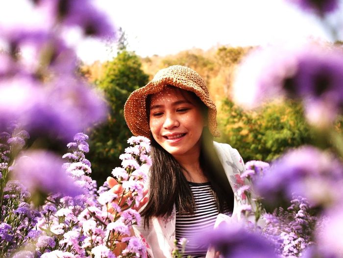 Portrait of smiling young woman against purple flowering plants