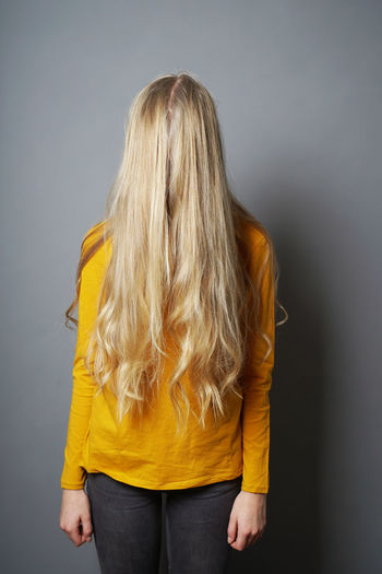 Teenage girl with blond hair standing against gray background