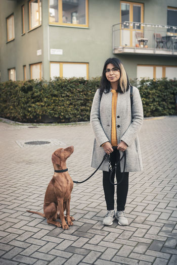 Portrait of young woman standing with dog on footpath