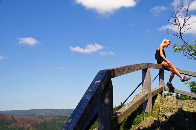 Woman sitting at railing against blue sky