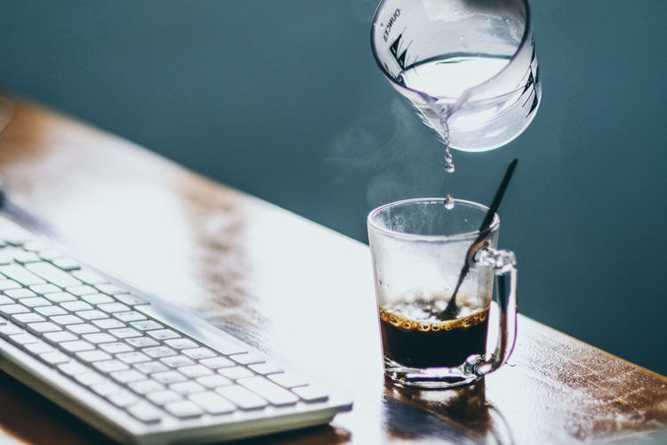 Water pouring in coffee cup by keyboard on table