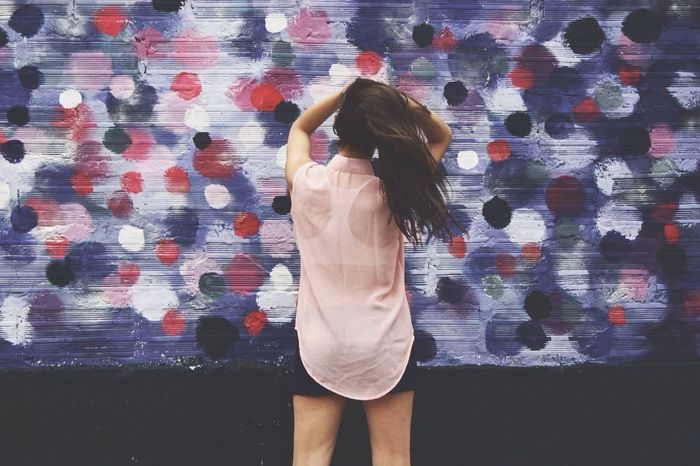Rear view of woman with arms raised holding hair against graffiti wall
