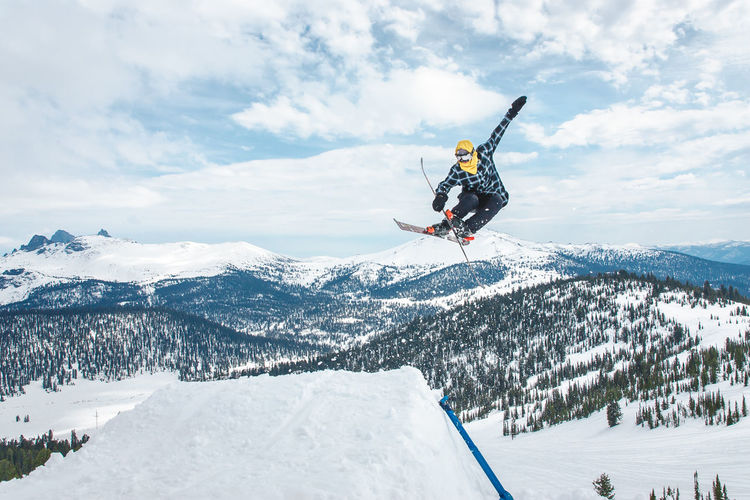 Full length of person jumping while skiing at snow covered mountains against sky