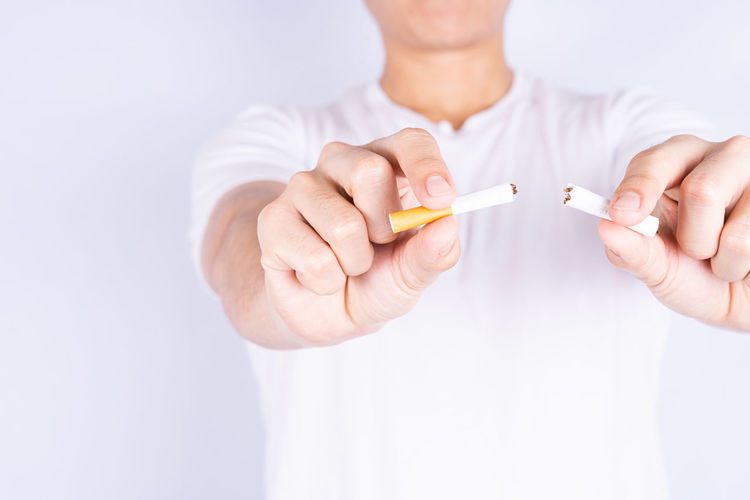 Close-up of hand holding cigarette over white background