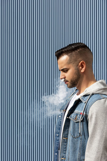 Young man smoking with an electronic cigarette over blue background