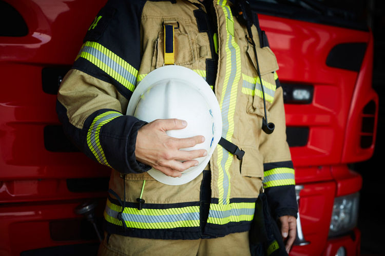 Midsection of female firefighter holding helmet while standing at fire station