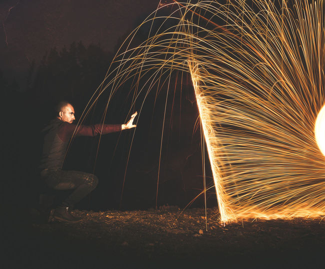 Man gesturing while crouching by sparks at night