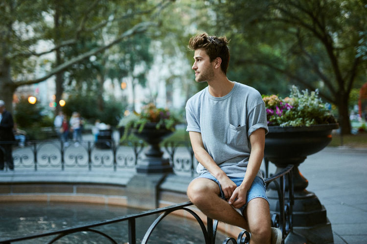Young man sitting by fountain at park