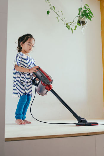 Cute little girl cleaning wooden floor with vacuum cleaner