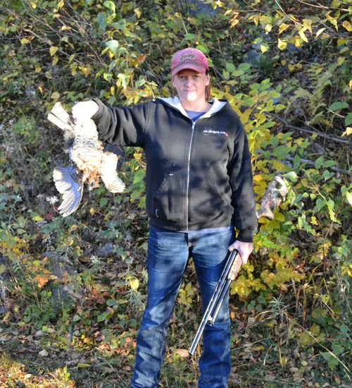 Portrait of female hunter with shotgun in one hand showing hunted partridge