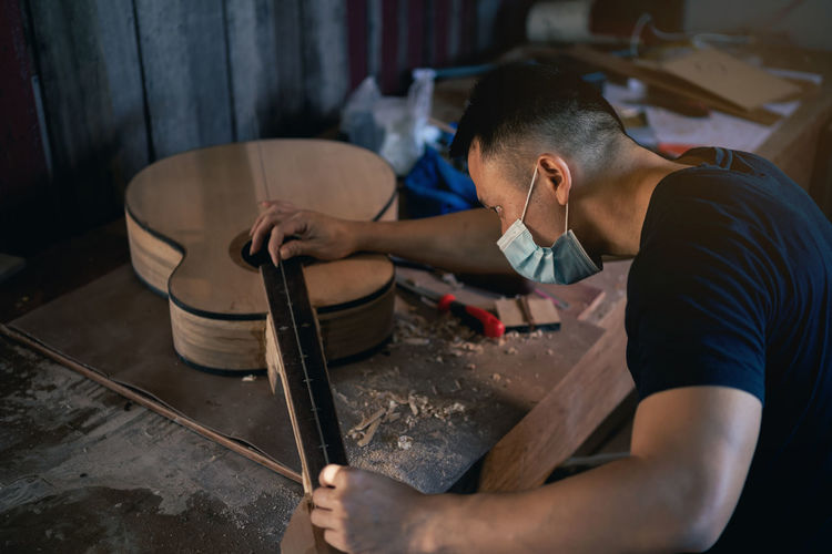 Man wearing mask making guitar at workshop