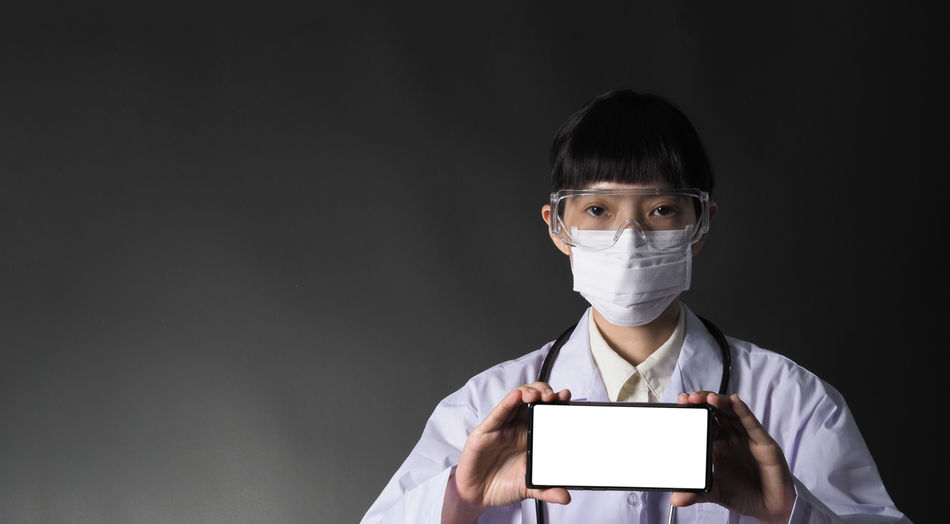 Portrait of doctor showing smart phone against black background